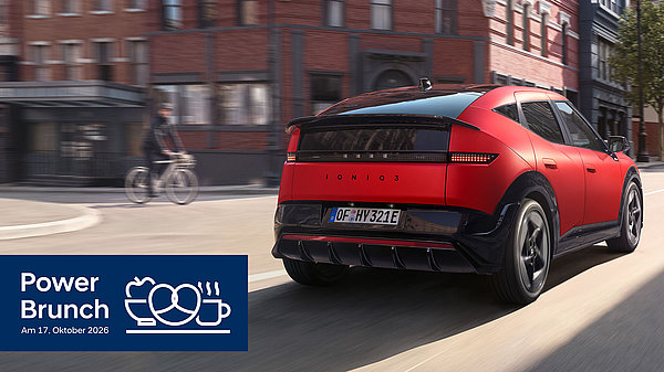 Ein roter Hyundai IONIQ 3 mit schwarzem Dach und Heckspoiler fährt, von hinten gesehen, durch eine Straße mit Backsteingebäuden, im Hintergrund ein Radfahrer. Unten links ein blaues Logo „Power Brunch – Am 17. Oktober 2026“ mit Symbolen von Teller, Brezel und Kaffeetasse.